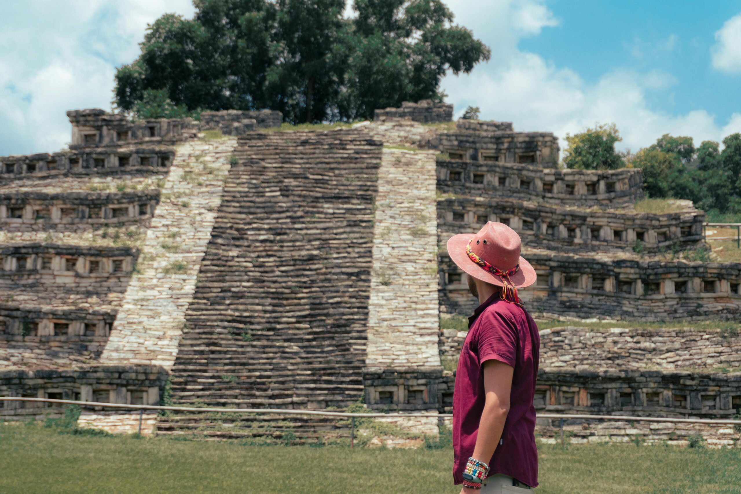 A man in a hat and pink shirt stands in front of a pyramid